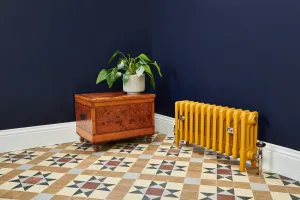 Low Mercury 4 column cast iron radiator in mustard yellow on feet, with nickel Windsor valve, against navy walls on a Victorian tiled floor.
