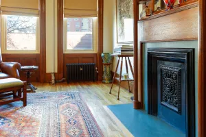 A plain Mercury 4 Column cast iron radiator in Matt Black under a panelled sash window, beside a fireplace and patterned rug.