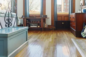 A low Mercury 4 Column cast iron radiator in Matt Black under a bay window, beside a wooden chest of drawers on an oak floor.