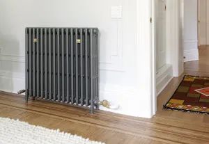 Plain four-column Mercury cast iron radiator in Astral Grey Mid on feet, with brass valve and wall stays, on a parquet floor by a doorway.