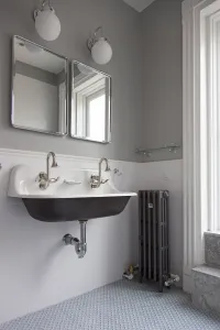 Plain Mercury 4 Column 860mm cast iron radiator in Astral Grey Mid on feet beside a double trough basin in a grey and white tiled bathroom.