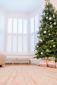 Low white Mercury 6 Column cast iron radiator under a shuttered bay window, beside a decorated Christmas tree, wrapped gifts and a rug.