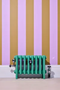 Low Mercury 6 Column cast iron radiator in green Little Greene Woodland on feet, with chrome valves, against lilac and ochre striped wallpaper.