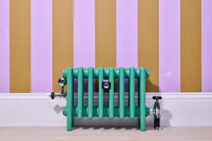 Low Mercury cast iron radiator on feet in Little Greene Woodland green, with chrome valves, against lilac and ochre striped wallpaper.