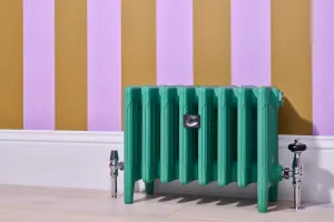 Low Mercury 6 column cast iron radiator in green Little Greene Woodland on feet, with chrome valves, against lilac and mustard striped wallpaper.