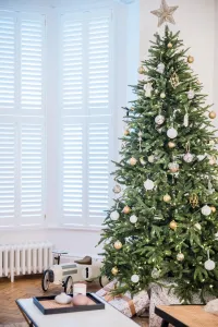 A low, plain white Mercury 6 Column cast iron radiator under shuttered bay windows, beside a Christmas tree and a toy car on a parquet floor.