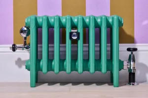 Low Mercury 6 Column cast iron radiator on feet in Little Greene Woodland green, with chrome valves and stay, against lilac and ochre striped wall.