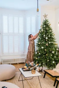 A low white Mercury 6 Column cast iron radiator under shuttered bay windows beside a decorated Christmas tree on a herringbone floor.