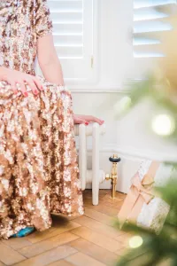 A low plain white Mercury cast iron radiator on feet with a brass angled valve, beside a woman in a gold sequin dress and a wrapped gift.
