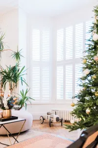 A low white Mercury 6 column cast iron radiator under shuttered bay windows, beside a Christmas tree and a toy car on a parquet floor.