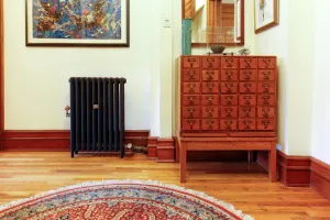 Plain Mercury cast iron radiator in Matt Black on feet, side valve, on a wooden floor beside an oak card-index cabinet and a round rug.