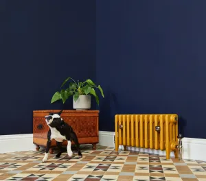 Low plain Mercury 4 column cast iron radiator in mustard yellow on feet with a Windsor valve, against navy walls on Victorian floor tiles.