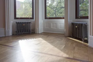 Two plain Mercury 4 Column cast iron radiators in Astral Grey Mid with brass valves, beneath bay windows above a parquet floor.