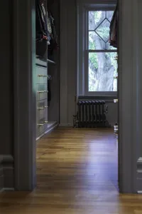 A low plain Mercury 4 Column cast iron radiator in Astral Grey Mid with brass valves beneath a window, seen through a doorway past wardrobes.