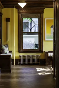 A low plain Mercury 4 Column cast iron radiator in a silver metallic finish beneath a wooden sash window, between window seats on herringbone floor.