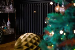 Plain Mercury cast iron radiator in Matt Black against a dark wall, beside a drinks trolley, with a lit Christmas tree in the foreground.