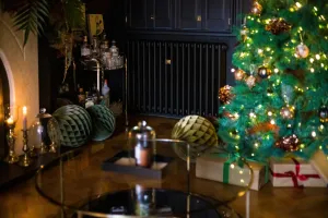 Mercury 4 Column cast iron radiator in Matt Black beneath dark cabinets, behind a drinks trolley and a lit Christmas tree with presents.
