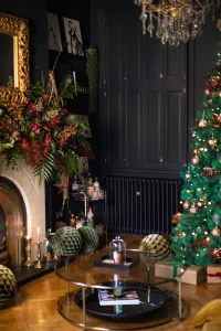 Plain Mercury 4 Column cast iron radiator in Matt Black under dark panelled cupboards, beside a Christmas tree and glass coffee table.