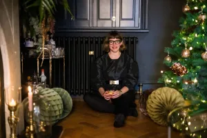 Plain Mercury cast iron radiator in Matt Black under dark cabinets, a woman seated on herringbone floor beside a Christmas tree and drinks trolley.