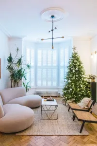 A low white Mercury 6 Column 360mm cast iron radiator beneath shuttered bay windows in a living room with a Christmas tree and parquet floor.