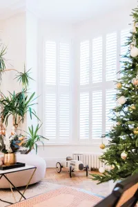 A low white Mercury 6 Column 360mm cast iron radiator under shuttered bay windows, beside a Christmas tree on a parquet floor.