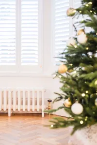 Low white Mercury 6 Column cast iron radiator with brass valve under shuttered window, herringbone floor and decorated Christmas tree