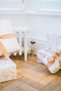 Low white Mercury 6 Column cast iron radiator on feet with a brass valve, beneath a window on a herringbone floor among wrapped gifts.