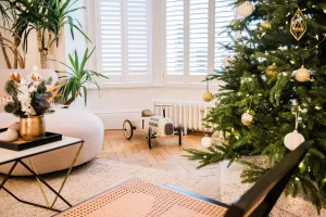 A low white Mercury cast iron radiator under a shuttered bay window, beside a decorated Christmas tree, toy car and herringbone parquet floor.