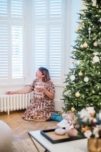 A low plain Mercury 6 Column cast iron radiator in Chalk under white-shuttered bay windows, beside a Christmas tree on a herringbone floor.