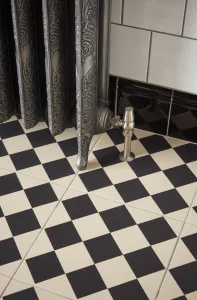 Ornate Rococo II cast iron radiator in Etch-Coated Polish on its feet, with a satin nickel angled valve, over black and cream chequered floor tiles.