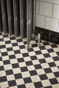 Ornate Rococo II cast iron radiator in Etch-Coated Polish on feet, with a satin nickel valve, on black and cream chequerboard floor tiles.