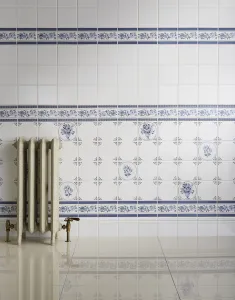 Ornate Rococo III cast iron radiator in Minster White on feet with brass angled valves, against blue and white floral tiles on a glossy floor.