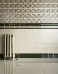Ornate Rococo III cast iron radiator in Minster White on feet with brass valves, against cream and patterned tiles above a glossy white floor.