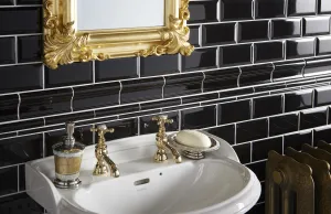 Ornate Rococo III cast iron radiator in Natural Brass beside a white basin with gold cross-head taps, black metro tiles and a gilt mirror.