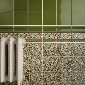 Ornate Rococo II cast iron radiator in a pale off-white finish with a brass angled valve, set against floral tiles and a green glazed dado.