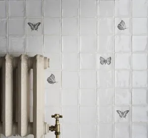 Ornate Rococo II cast iron radiator in Fossil with a brass crosshead valve, against white glazed tiles with black butterfly motifs.