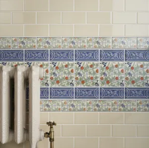 Ornate cream Rococo II cast iron radiator with a brass angled valve against cream metro tiles and bird-and-trellis border tiles.