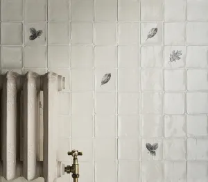 Ornate Rococo II cast iron radiator in Fossil beside a brass angled valve, against cream handmade tiles printed with leaves.