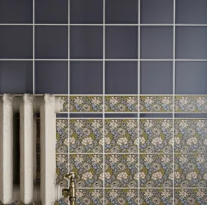 Ornate Rococo II cast iron radiator in an off-white finish with a brass angled valve, against grey and floral patterned wall tiles.