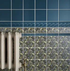 Ornate cream Rococo II 510mm cast iron radiator with a brass valve, against teal and floral-patterned wall tiles.