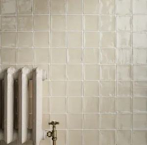 Ornate Rococo II cast iron radiator in Fossil, partly in view against handmade cream square wall tiles, with an antique brass angled valve.