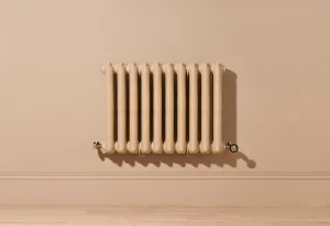 Wall-hung ornate Rococo II 660mm cast iron radiator in Farrow & Ball Planter No. G5 with brass valves, against a matching pink wall above a wooden floor.