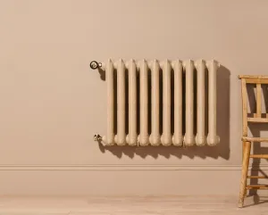 Ornate Rococo II 660mm cast iron radiator in Farrow & Ball Planter No. G5, wall-hung with brass valves, beside a wooden chair on a pale floor.