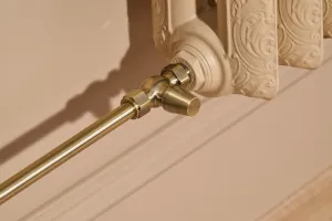 Close-up of an ornate Rococo II cast iron radiator in Farrow & Ball Planter No. G5 with an angled brass valve and pipe above a skirting board.