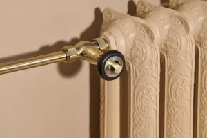 Close-up of an ornate Rococo II 660mm cast iron radiator in Farrow & Ball Planter No. G5, with an angled brass valve and pipe on a beige wall.
