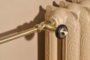 Close-up of an ornate Rococo II cast iron radiator in Farrow & Ball Planter No. G5 with a brass angled valve and dark wooden head.