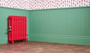 Ornate Rococo II cast iron radiator on feet in Benjamin Moore Heritage Red HC181, with valve, against green panelling on a parquet floor.