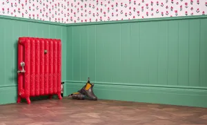 Ornate Rococo II cast iron radiator on feet in Benjamin Moore Heritage Red HC181 with brass valve, against green panelling on a parquet floor.