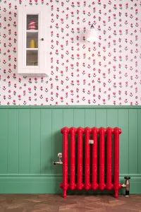 Ornate Rococo II cast iron radiator in Benjamin Moore Heritage Red HC181 on feet, with brass valves, against green panelling below floral wallpaper.