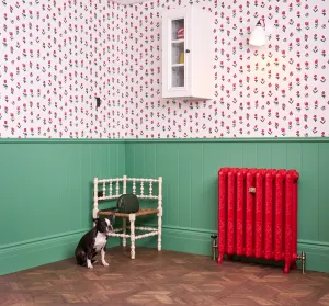 Ornate Rococo II cast iron radiator in Benjamin Moore Heritage Red HC181 on feet, with brass valves, against green panelling beside a dog and chair.